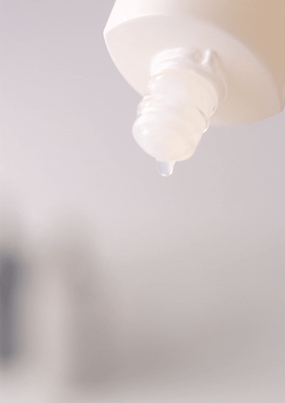 Lotion coming out of a glass dropper bottle against a blurred white background​