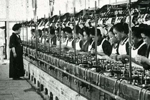 Many workers stand in line, spinning silk thread in a factory.
