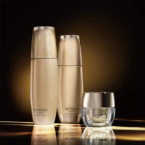 Two golden bottles and a jar set against dim, brown background